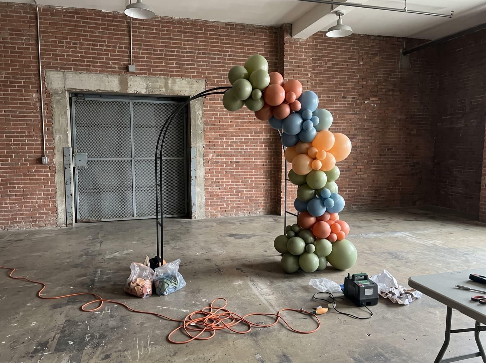 Organic balloon garland half-built on an arch frame in a loft before an event