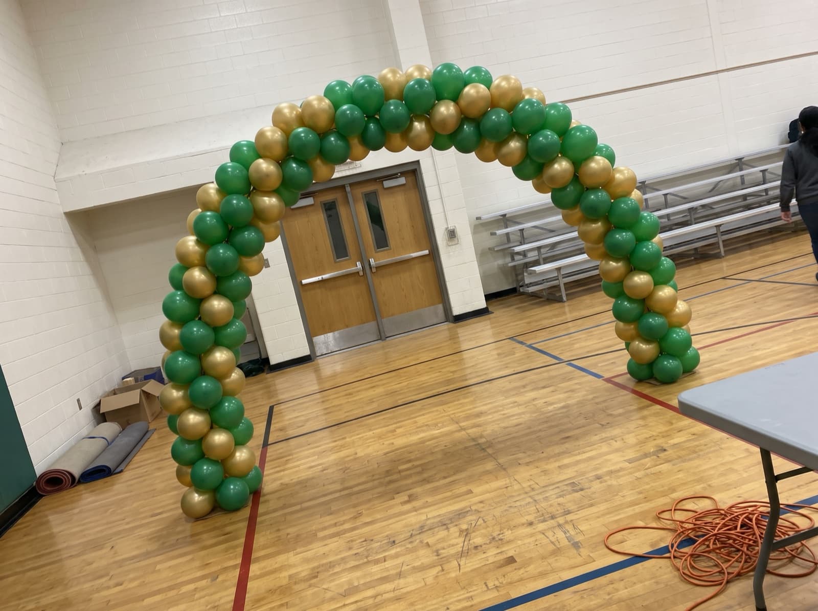 Spiral balloon arch in green and gold over a school gym entrance