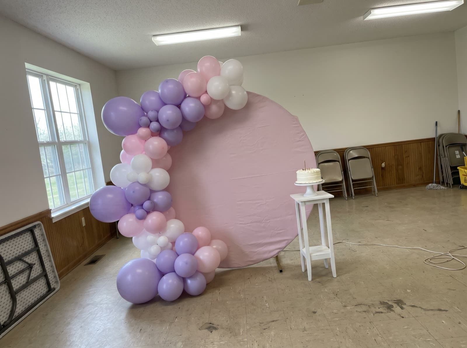Round balloon backdrop with a lavender and pale pink garland and a cake stand at a birthday party