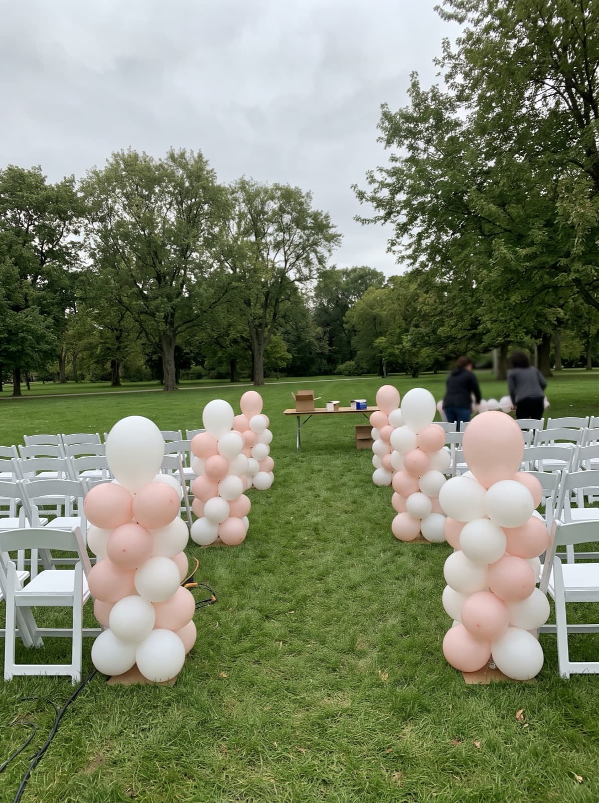 Organic balloon columns in white and blush lining a park ceremony aisle
