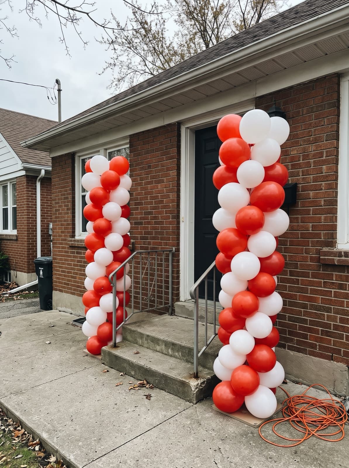 Pair of red and white spiral balloon columns at a bungalow front door