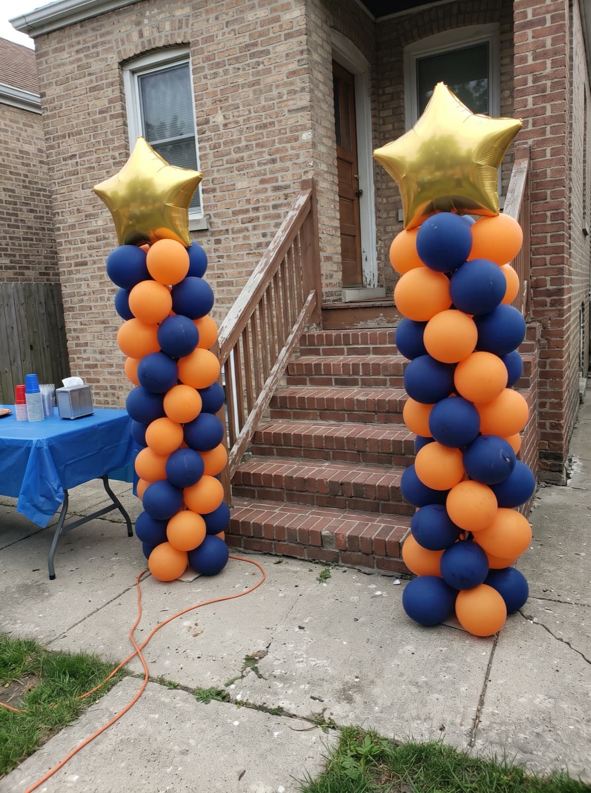 Pair of spiral balloon columns in navy and orange with gold star toppers beside the back steps of a Chicago bungalow