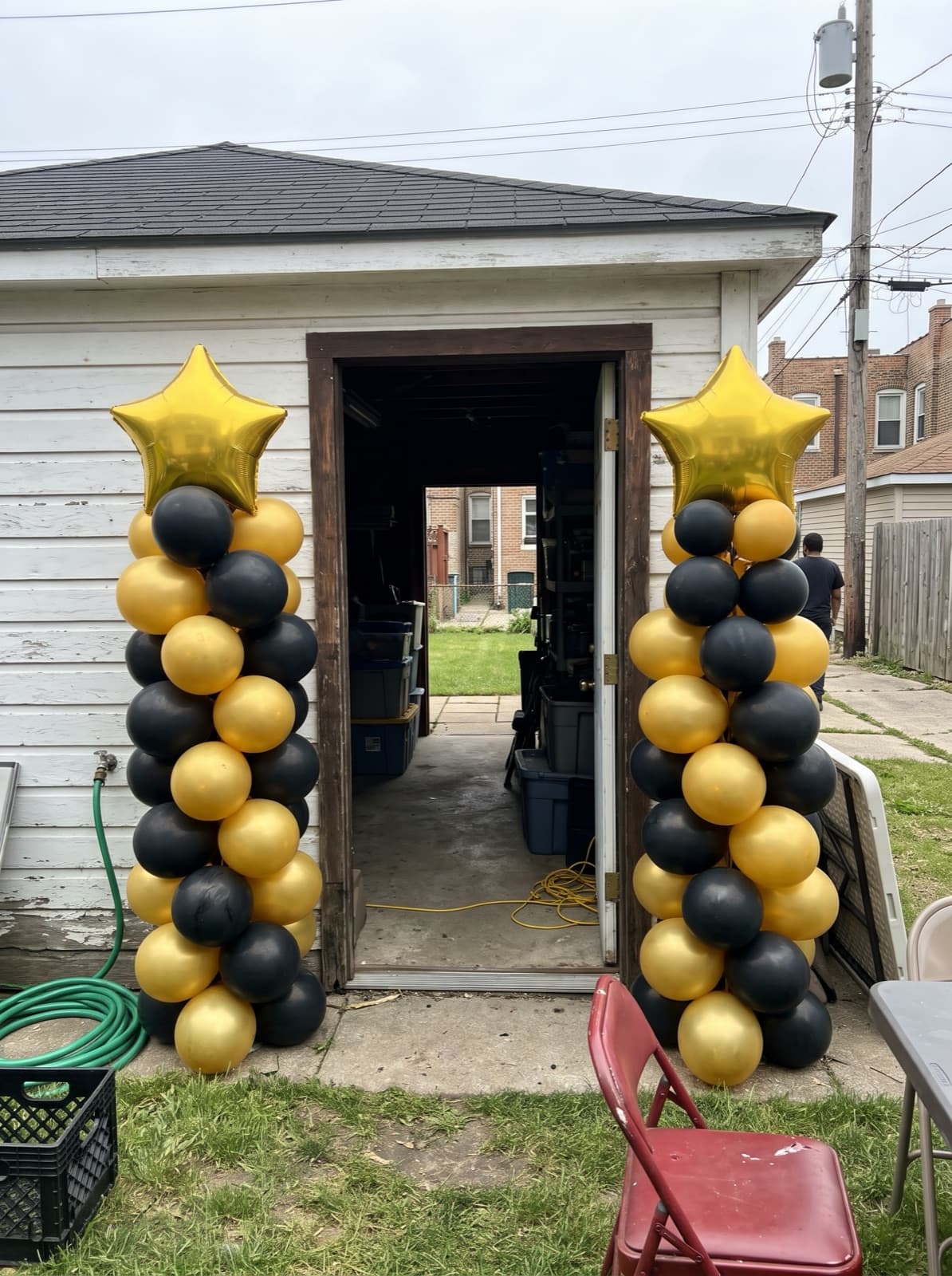 Black and gold balloon columns with star toppers beside an alley garage