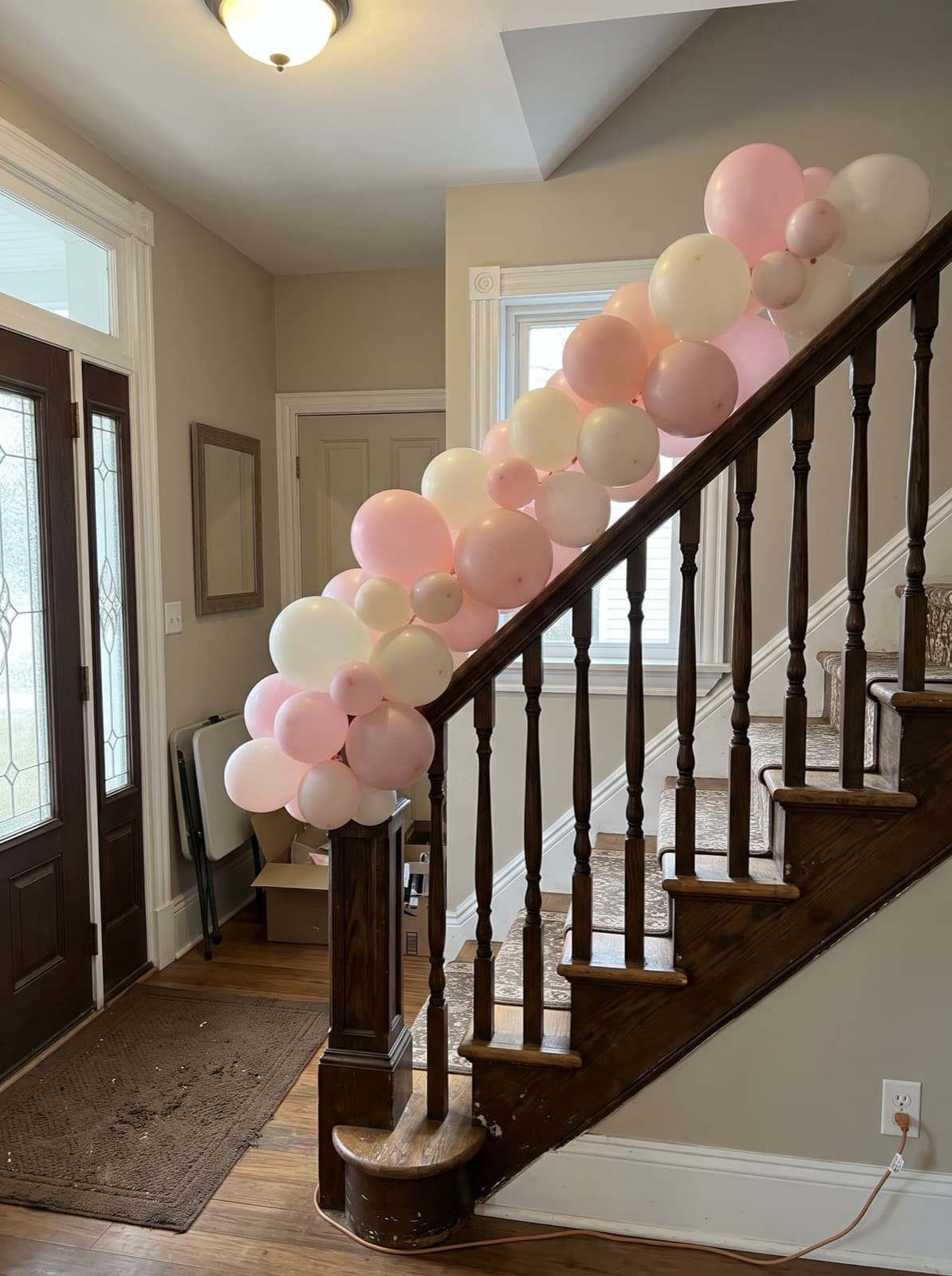 Blush and white balloon garland down a dark oak staircase banister