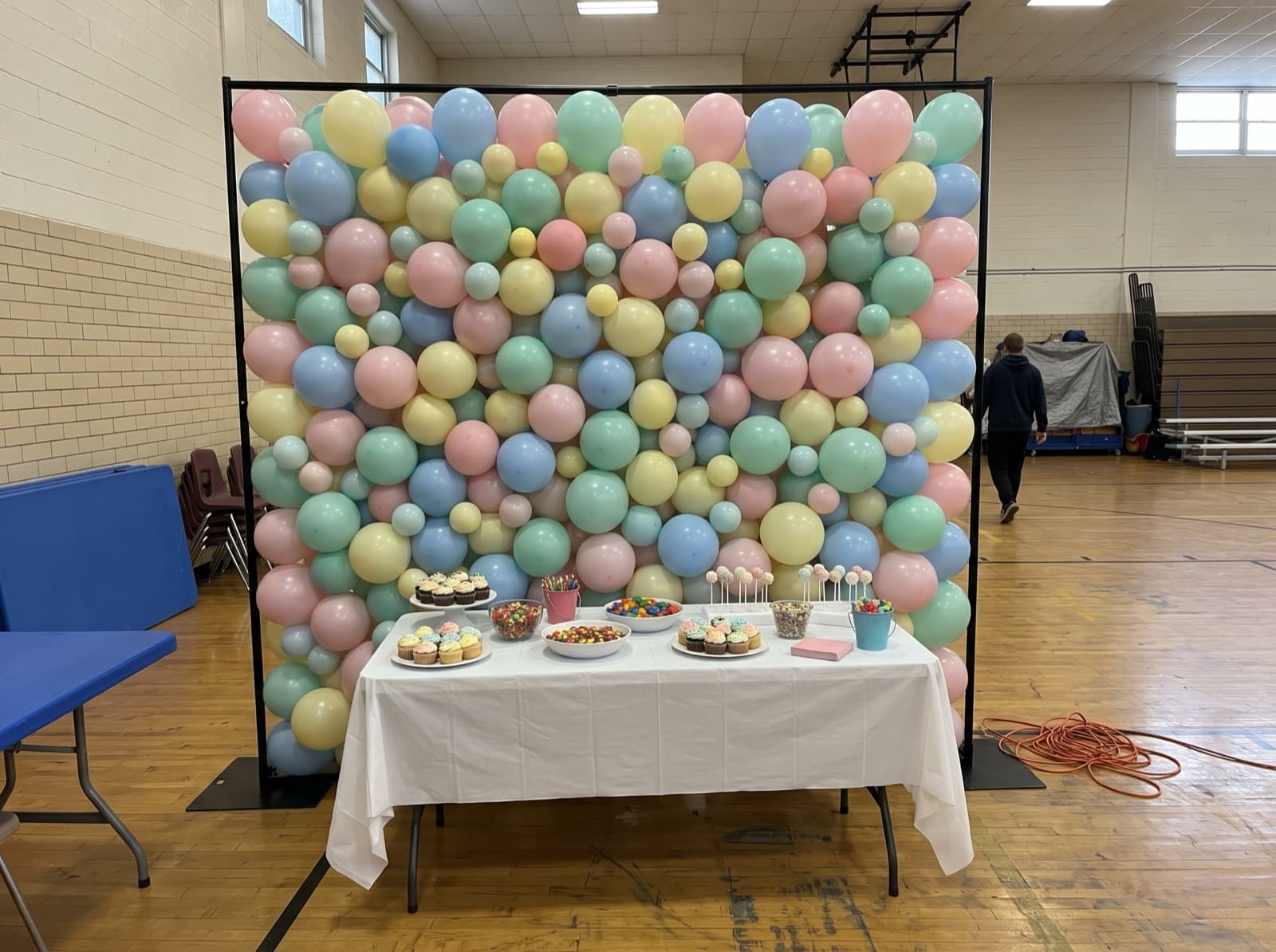 Square framed balloon wall in pastel colors behind a dessert table