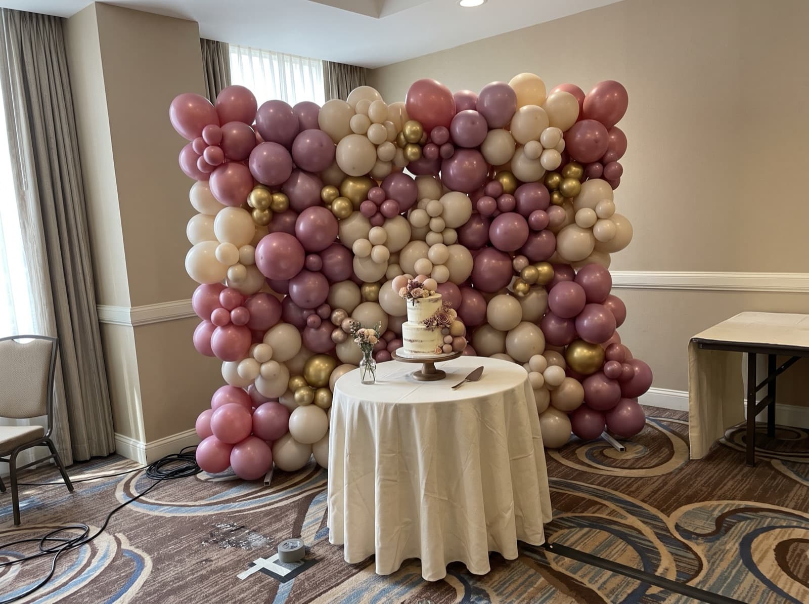 Organic balloon wall in dusty rose, mauve and cream behind a cake table
